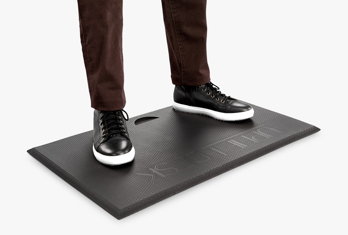 A man stands on an anti-fatigue standing mat